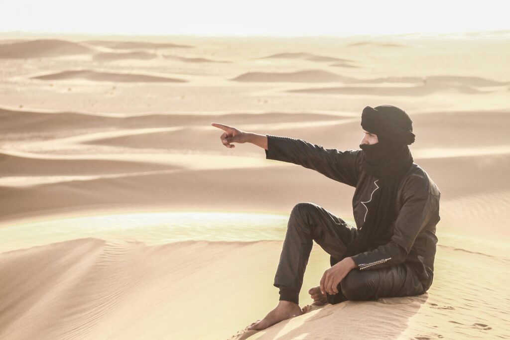 pexels photo 18884469 18884469 Man in traditional attire pointing across dunes in the Sahara Desert.