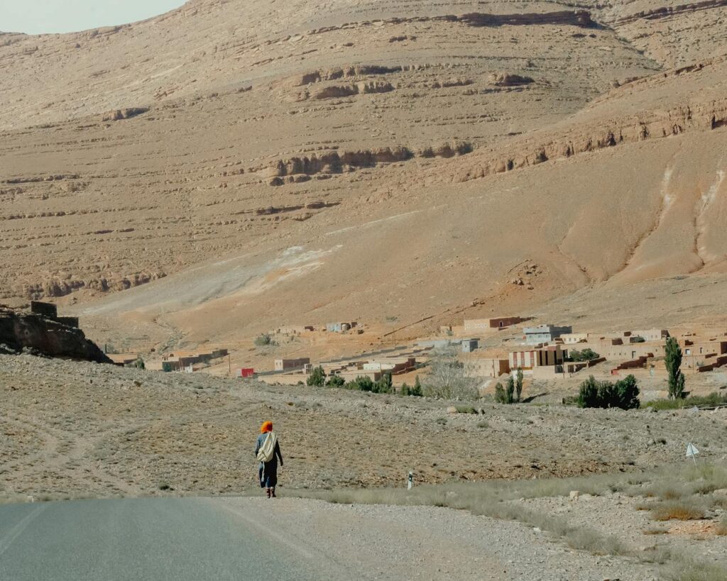 pexels photo 34100479 A person walks on a road towards a traditional village in Imilchil, Morocco, framed by the Atlas Mountains.