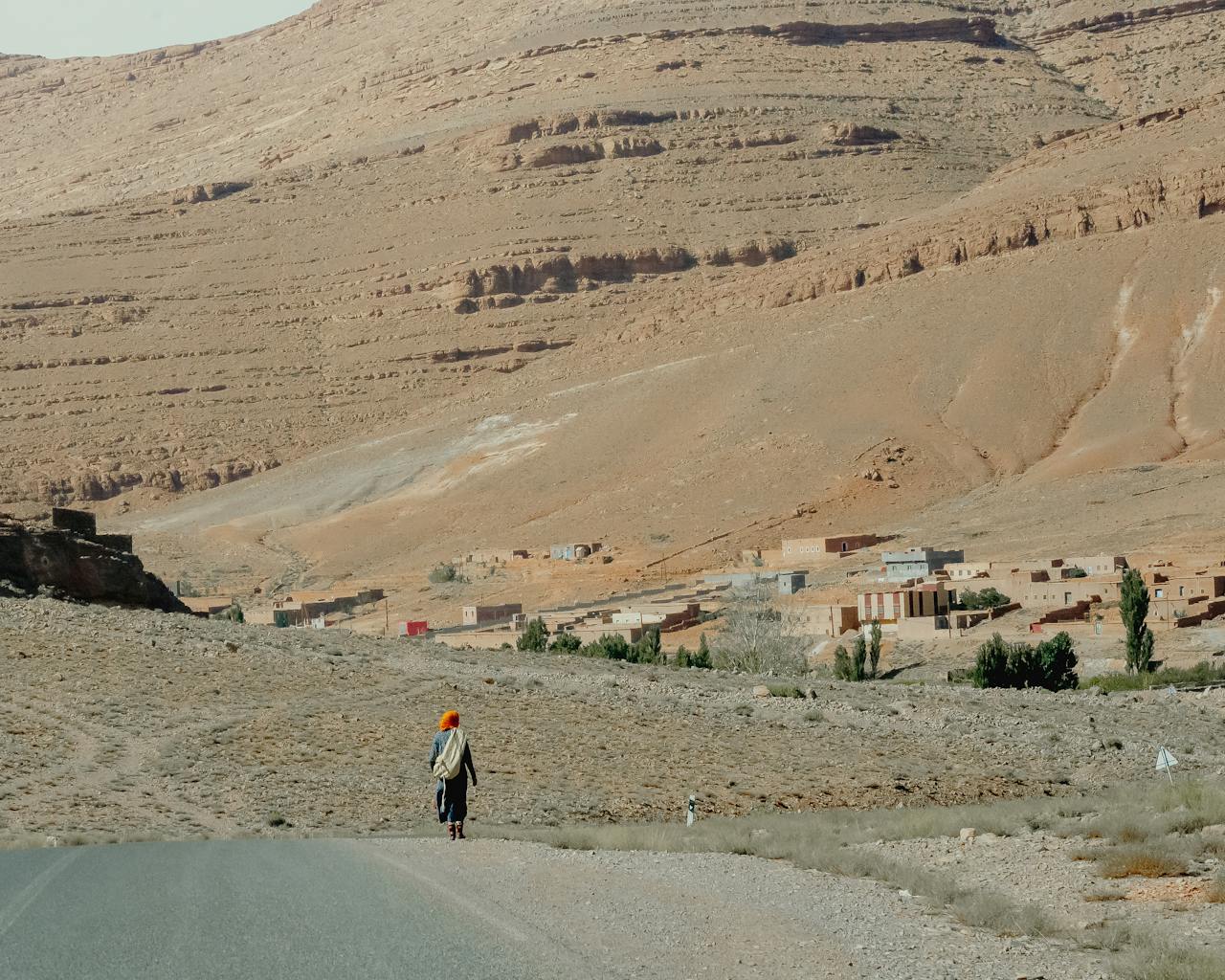 A person walks on a road towards a traditional village in Imilchil, Morocco, framed by the Atlas Mountains.