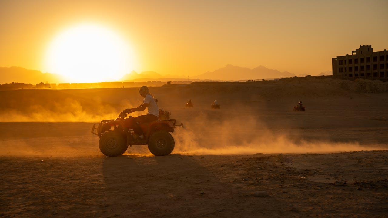 ATV riders explore the desert landscape at sunset, creating a scene filled with dust and motion.